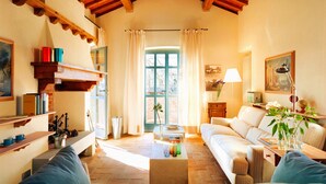 A cozy living room with a fireplace, a sofa, a coffee table, and a window with curtains. - Villa Nocciolo in most Exclusive Borgo in Tuscany (Pian di Sco)
