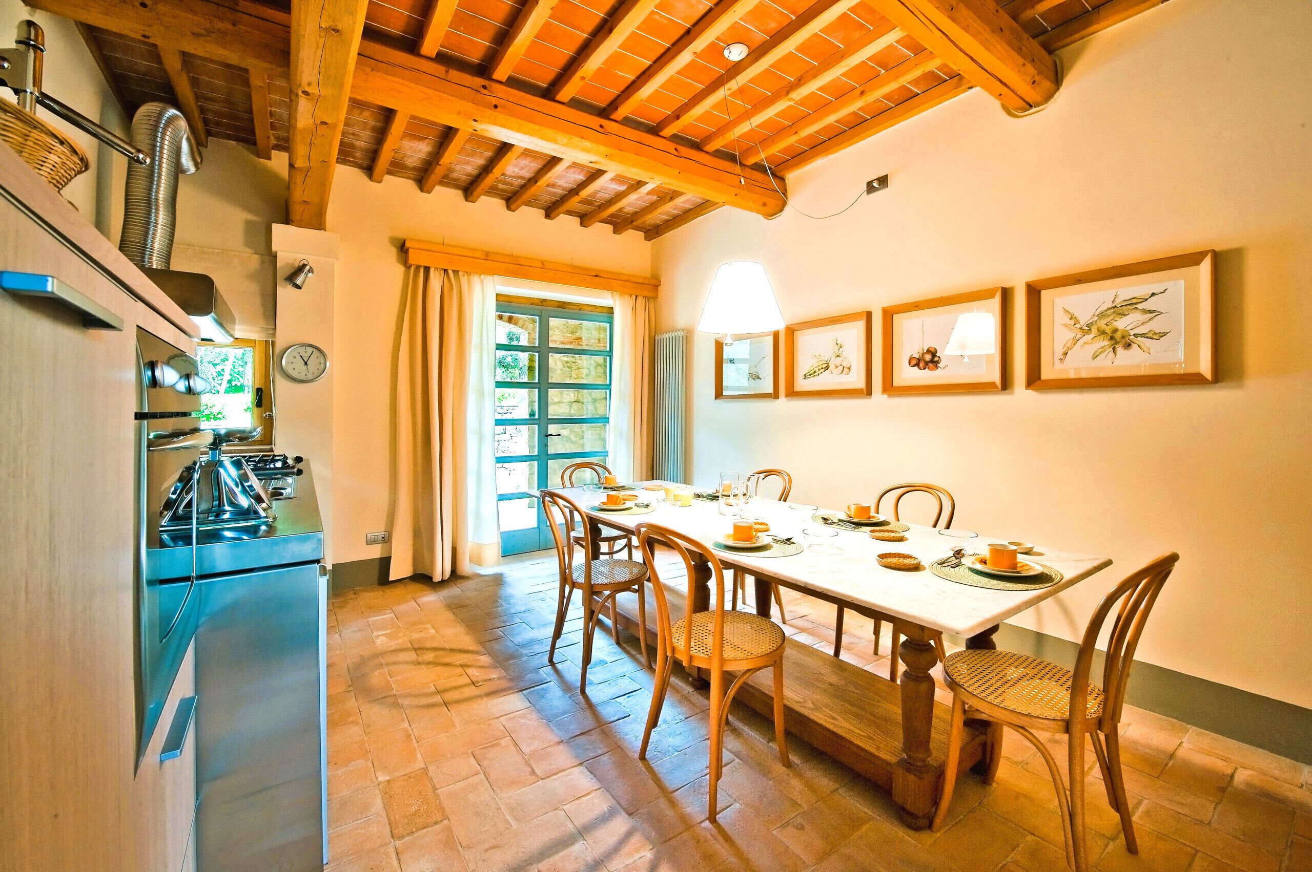 Zona pranzo con tavolo in legno, sedie e vista sull'esterno attraverso una finestra.