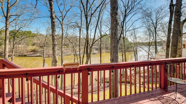 Een houten terras met een rode balustrade met uitzicht op een natuurlandschap met bomen en een waterpartij.