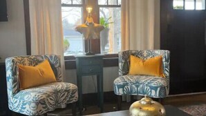 Una habitación con dos sillones estampados, una mesita con un libro y un objeto decorativo, y una ventana con cortinas.