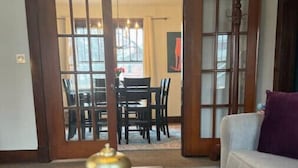 Una sala de estar con un sofá, una mesa de centro con un libro y un objeto decorativo, y vistas a un comedor a través de un ventanal.