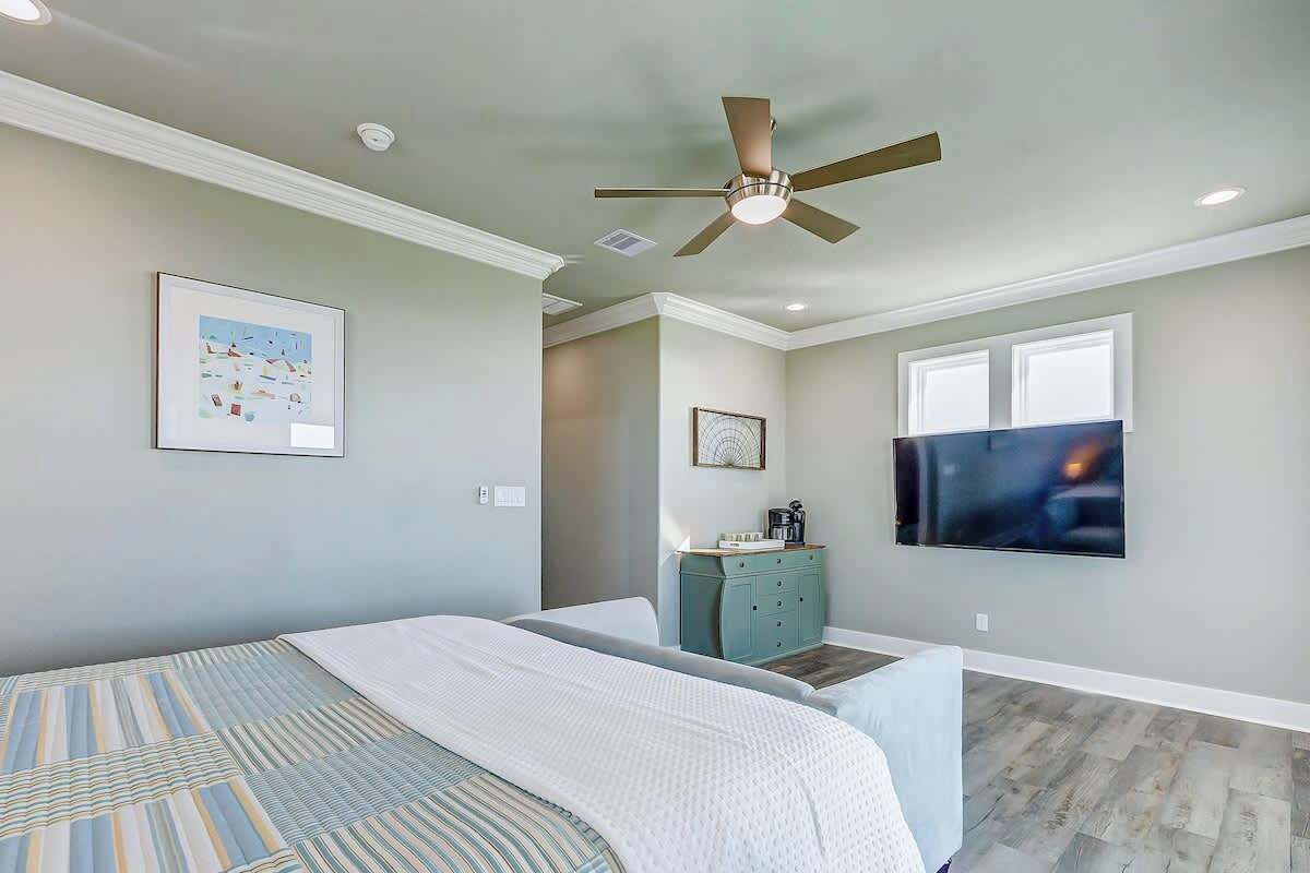 A bedroom with a bed, a ceiling fan, a dresser, a television, and artwork on the walls.