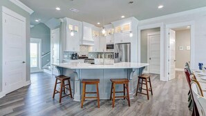 A spacious kitchen with a large island, white cabinetry, and a herringbone tile backsplash.