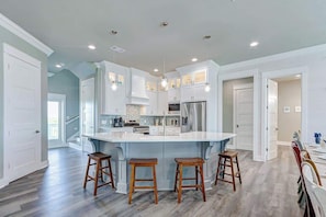 A spacious kitchen with a large island, white cabinetry, and a herringbone tile backsplash.
