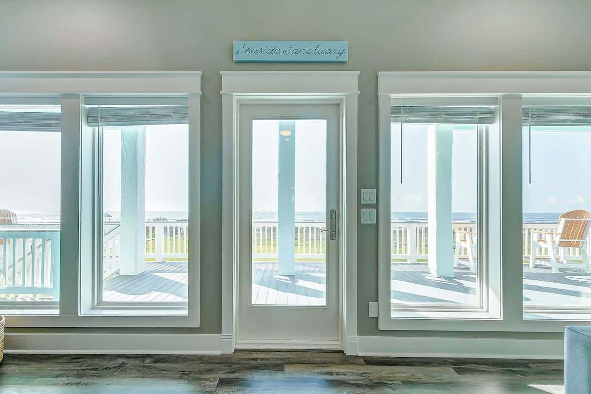 Una habitació amb tres grans finestres, una porta blanca i un rètol sobre la porta que diu "Seaside Sanctuary".