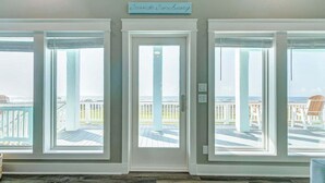 A room with three large windows, a white door, and a sign above the door that reads "Seaside Sanctuary."