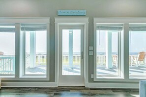 A room with three large windows, a white door, and a sign above the door that reads "Seaside Sanctuary."