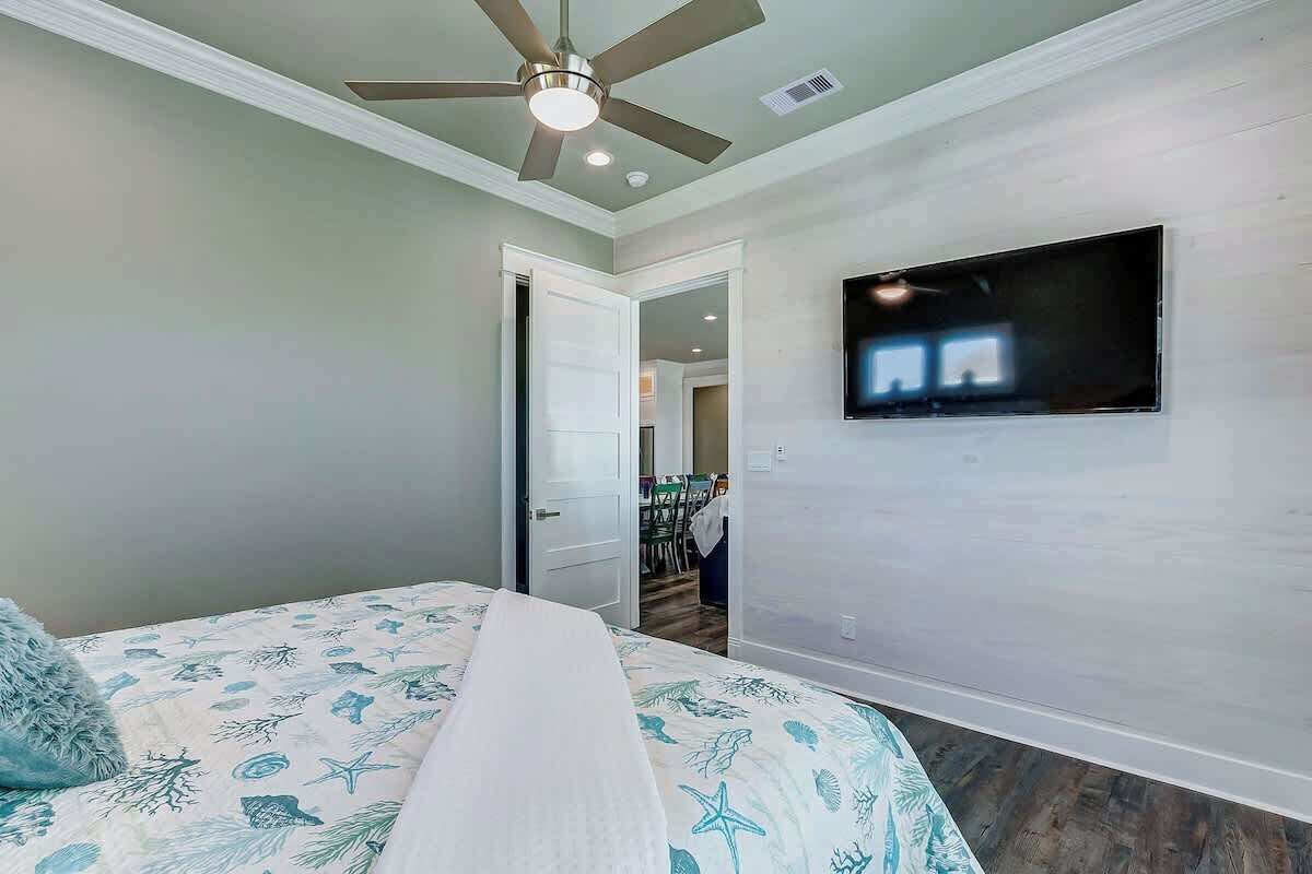 A bedroom with a bed, a ceiling fan, and a television mounted on the wall.