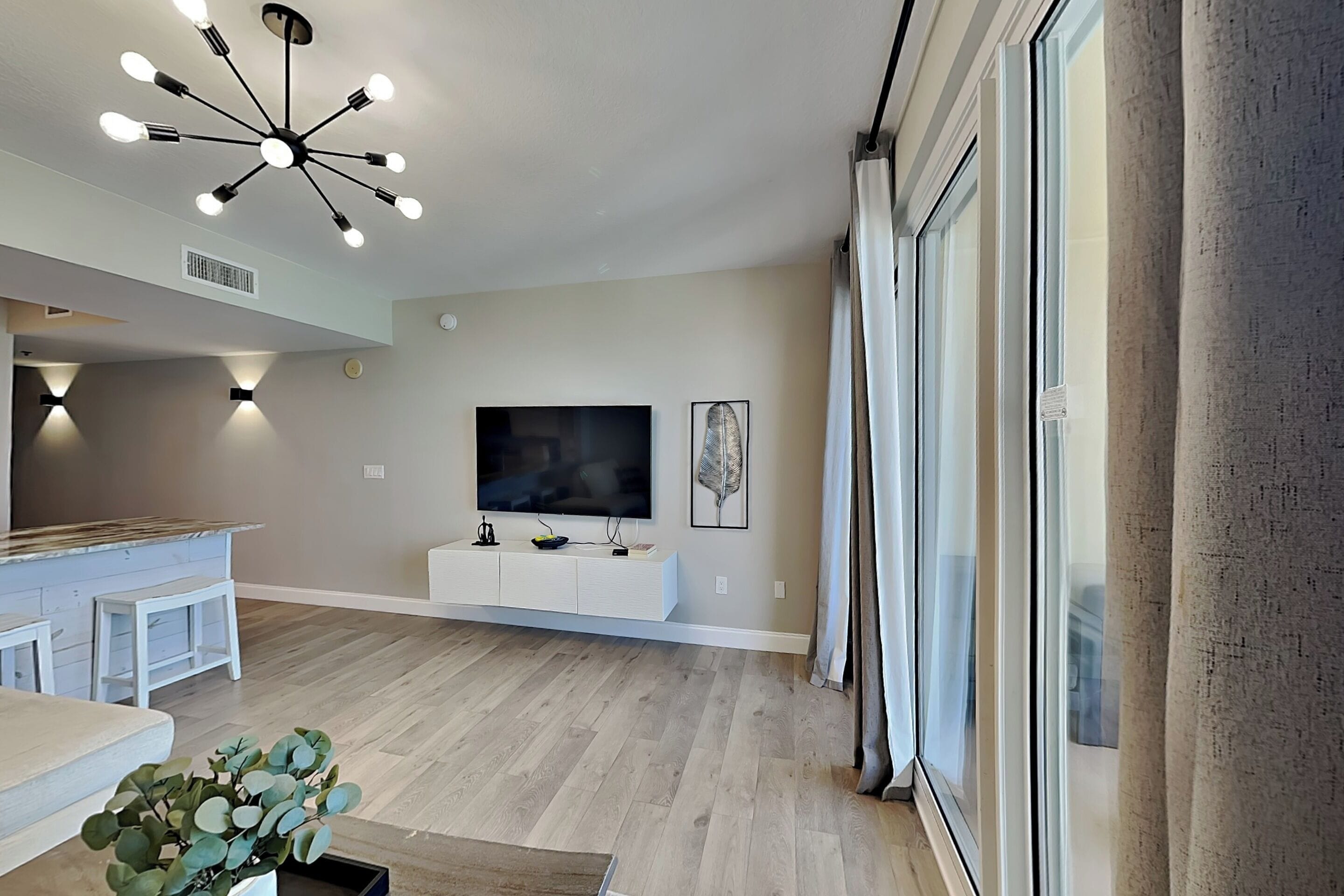 Uma sala de estar moderna com televisão, luminária no teto e uma janela grande com cortinas.