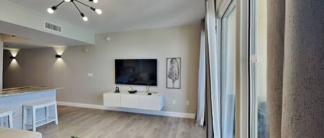 Uma sala de estar moderna com televisão, luminária no teto e uma janela grande com cortinas.
