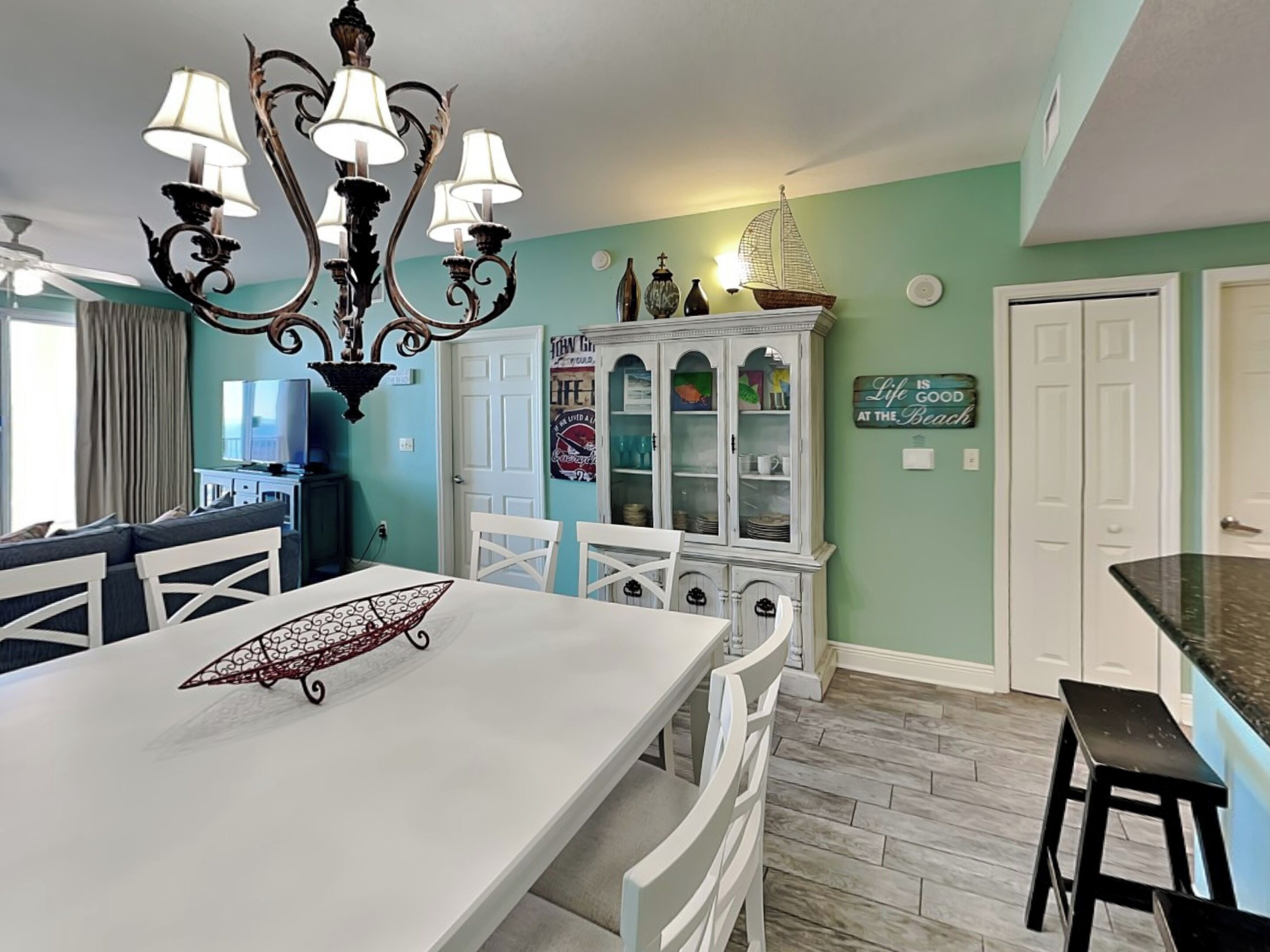 A dining area with a white table, chairs, and a chandelier. There is a cabinet with glass doors and a sign on the wall.