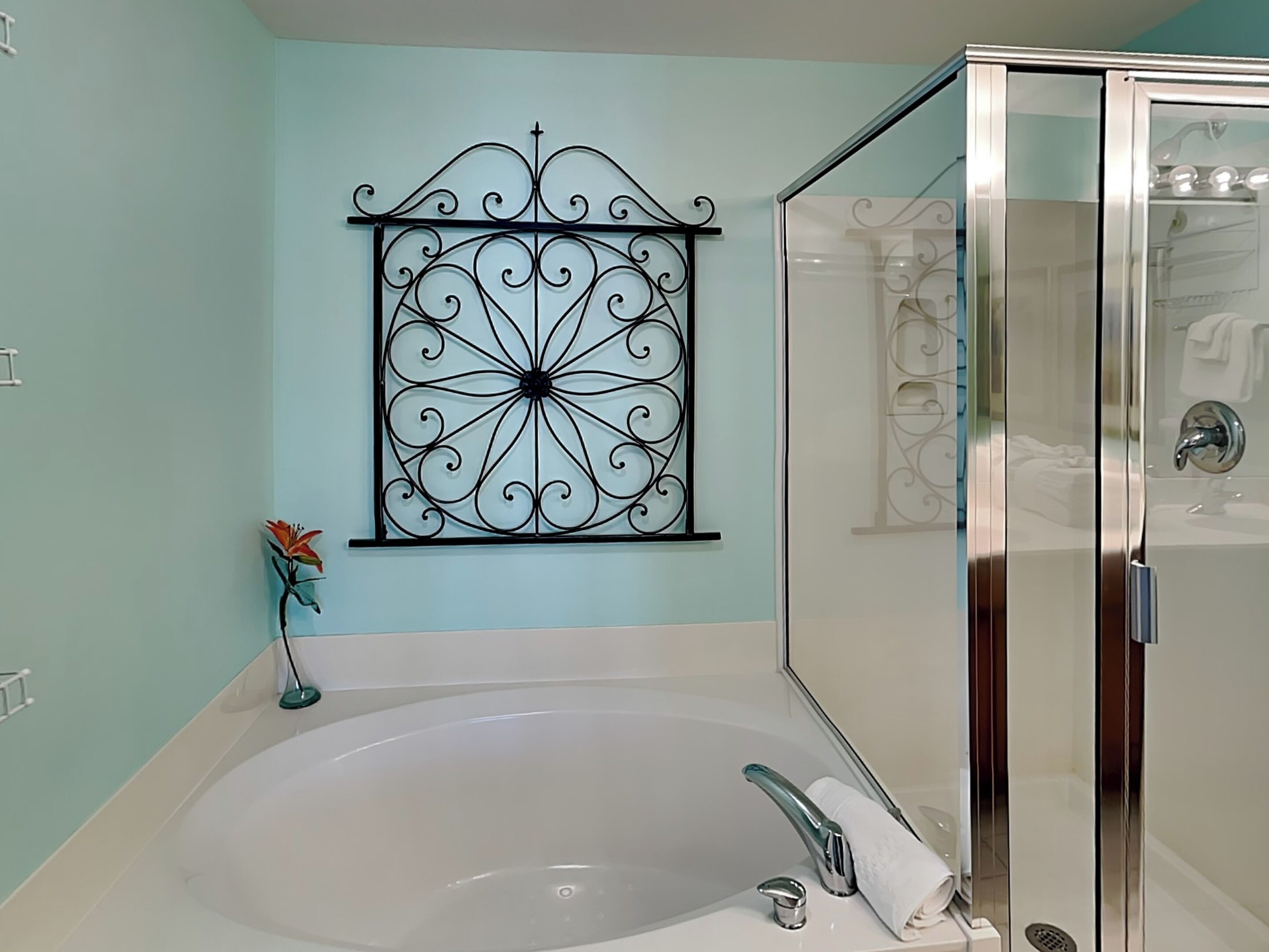 Ein Badezimmer mit einer großen Badewanne, einer Duschkabine aus Glas und einer dekorativen Metallwandgestaltung.