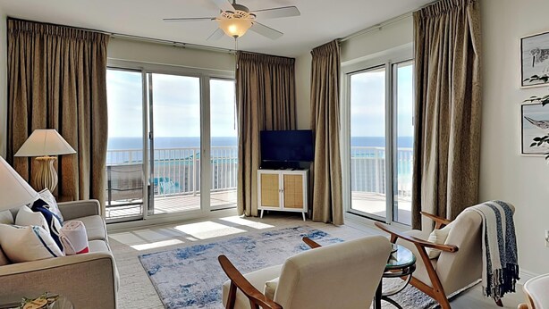 Ein geräumiges Wohnzimmer mit Balkon, Deckenventilator, Flachbildfernseher und Meerblick.