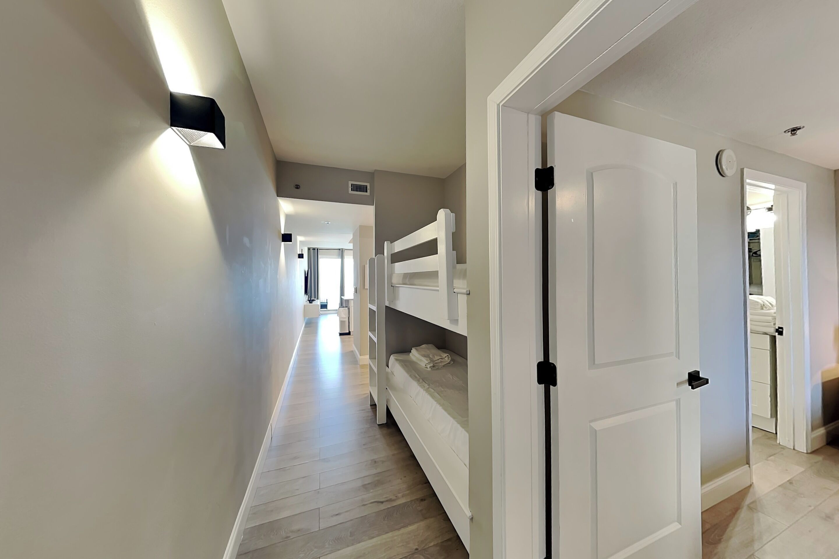 A hallway with bunk beds, a white door, and a light fixture.