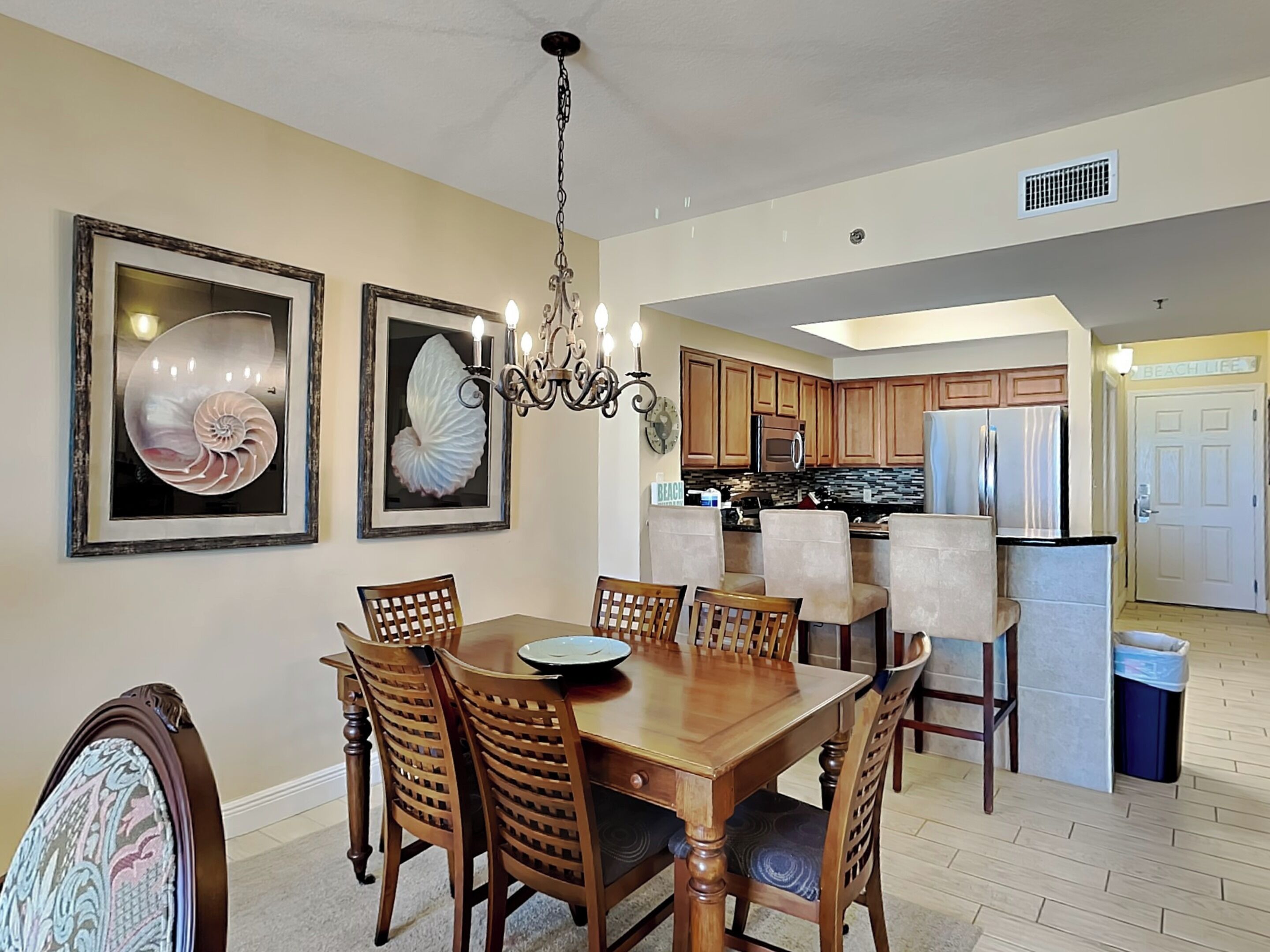 A dining area with a wooden table and chairs, a chandelier, and framed artwork on the walls.