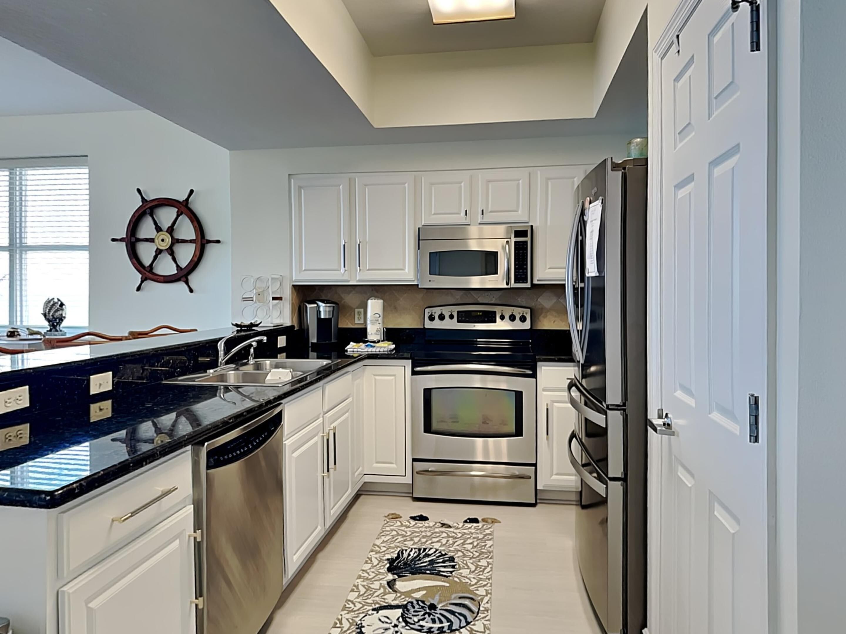 A modern kitchen with white cabinets, stainless steel appliances, and a decorative rug.
