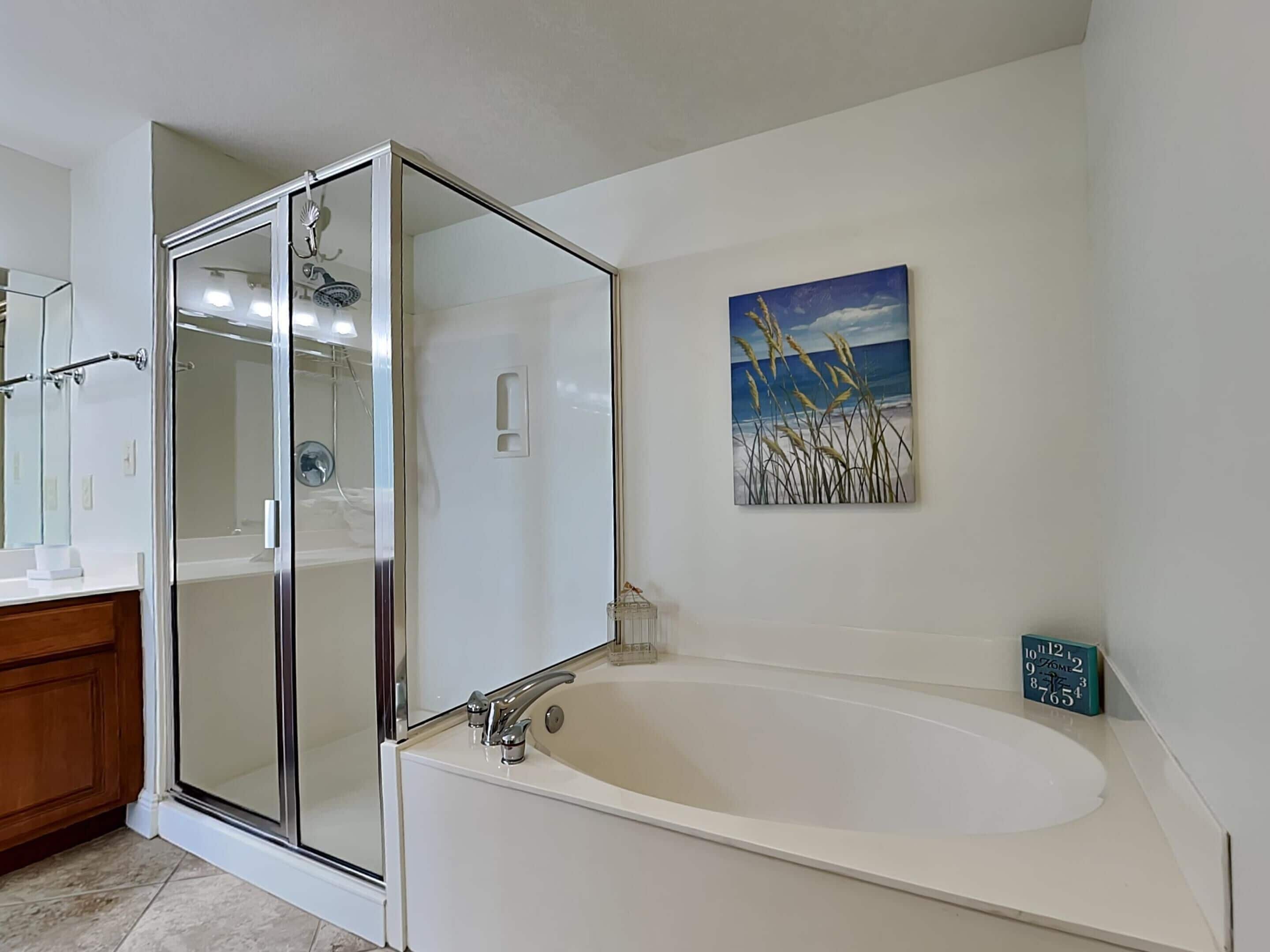 A modern bathroom with a glass-enclosed shower, a freestanding bathtub, and a painting of a beach scene.