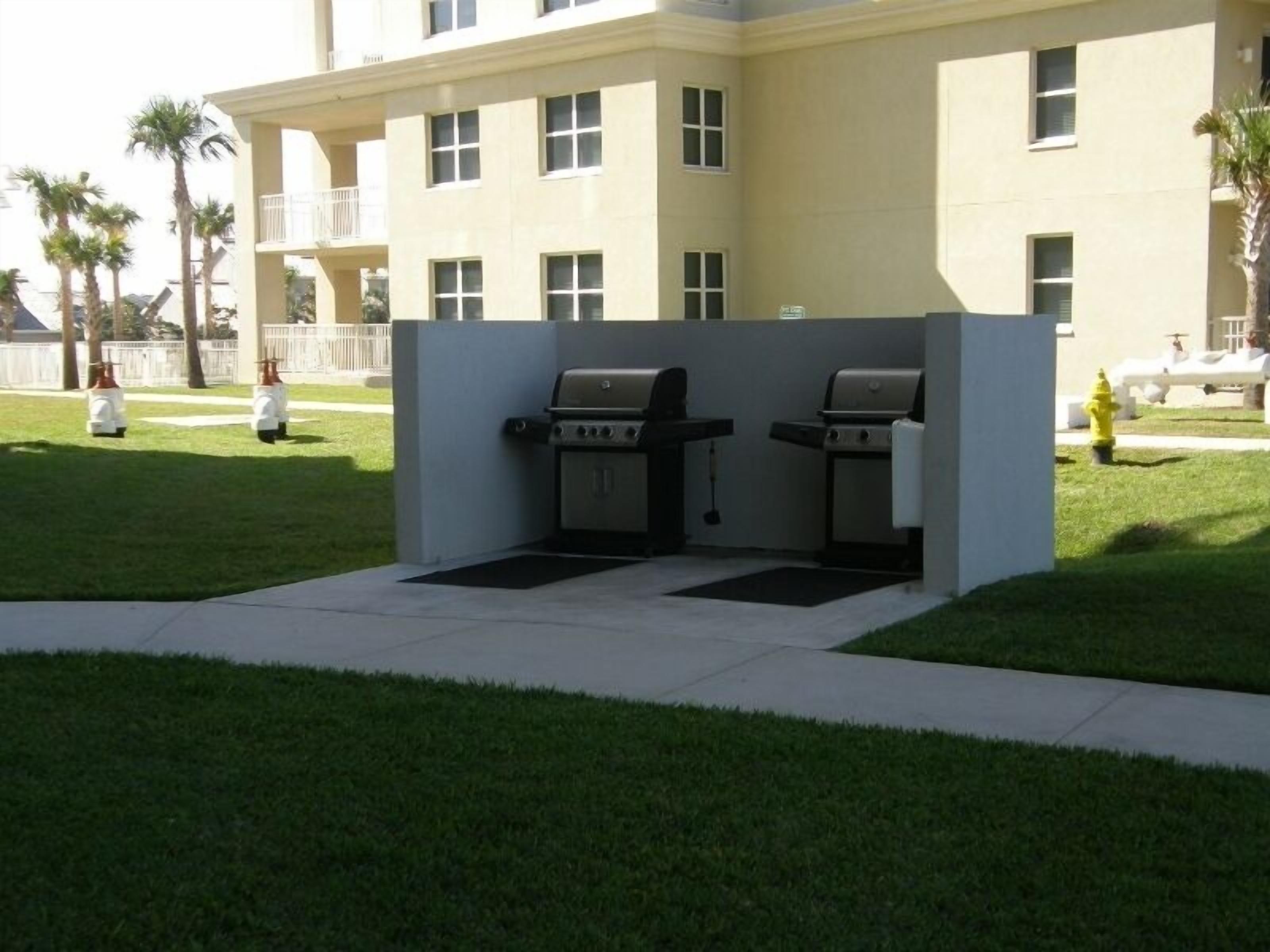 An outdoor grill area with two barbecue grills, a concrete pathway, and a building with multiple windows in the background.