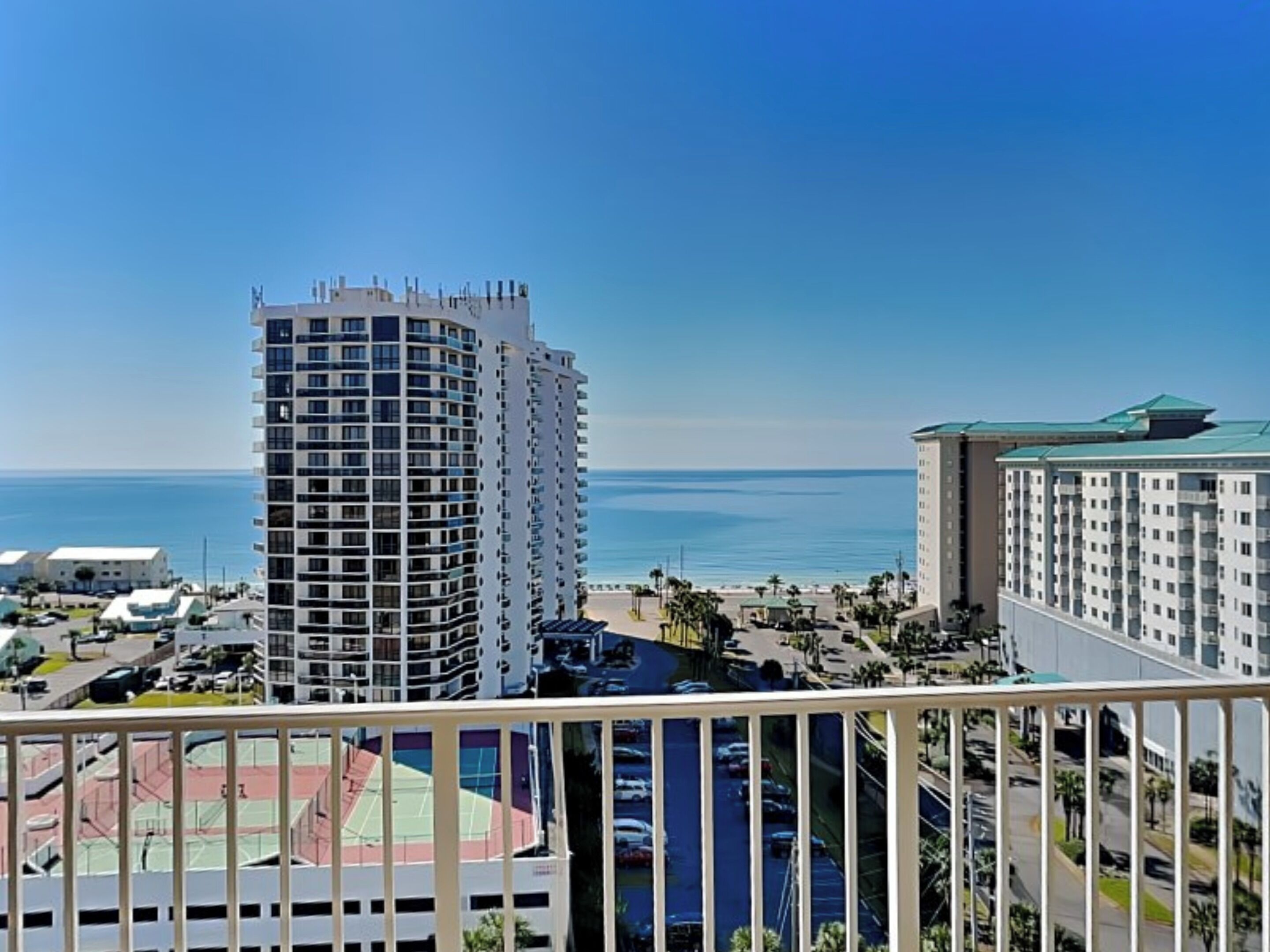 A high-rise hotel with multiple floors, a parking area, and a view of the ocean.