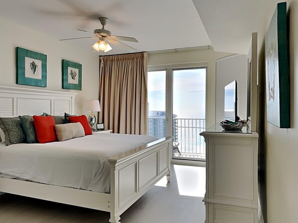 A bedroom with a bed, a ceiling fan, a window with curtains, and a view of the city. - Ariel Dunes by Southern Vacation Rentals (Miramar Beach)
