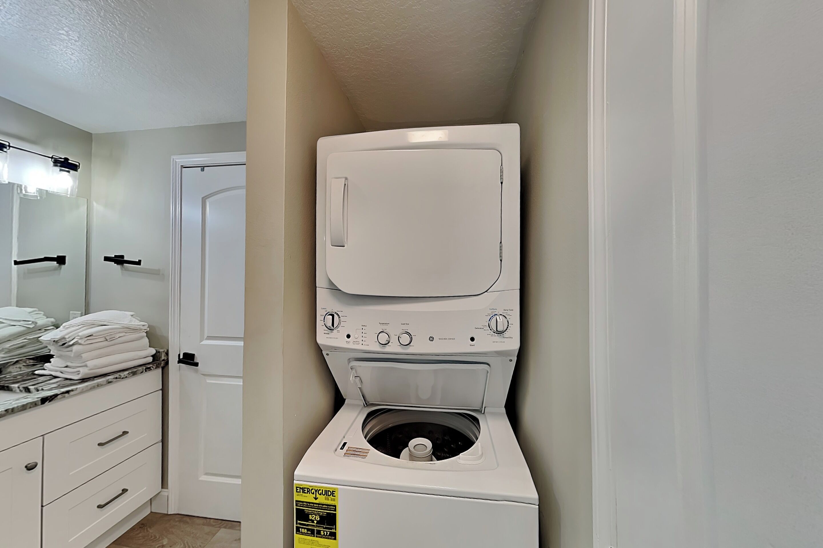 A compact washer and dryer unit with a control panel, a door, and a stack of folded towels on a counter.
