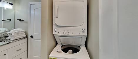A compact washer and dryer unit with a control panel, a door, and a stack of folded towels on a counter.