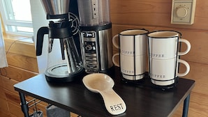 Eine Kaffeemaschine, zwei Kaffeetassen und ein Löffel auf einem Holztisch in einer Küche.