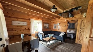 Ein gemütliches Blockhaus-Interieur mit Holzbalkendecke, einer Couch, einem Esstisch und einem Bett.
