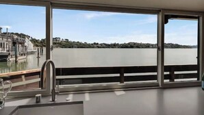 A modern room with large windows overlooking a body of water and a distant shoreline. - Floating condo 'C' on Sausalito's Richardson Bay (Mill Valley)