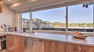 Cocina moderna con armarios de madera, electrodomésticos de acero inoxidable y un amplio ventanal con vistas a un edificio y árboles.