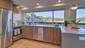 A modern kitchen with wooden cabinets, stainless steel appliances, and a large window offering a view of buildings and hills. - Floating condo 'C' on Sausalito's Richardson Bay (Mill Valley)