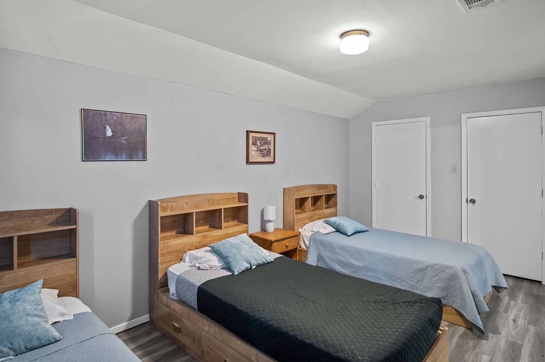 Een slaapkamer met twee bedden, houten hoofdborden, een nachtkastje, een lamp en twee deuren.