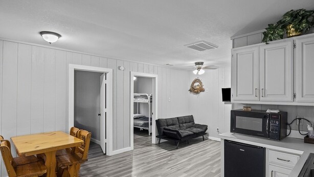 Une pièce compacte comprenant une table à manger en bois, un canapé, un lit superposé et une kitchenette équipée d’un four à micro-ondes et d’un réfrigérateur.