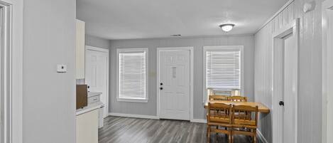 A hallway with a wooden dining table and chairs, white doors, and a ceiling vent.