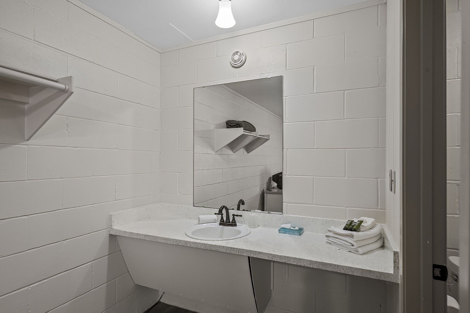 A modern bathroom with white tiled walls, a white sink, a mirror, and a towel rack.