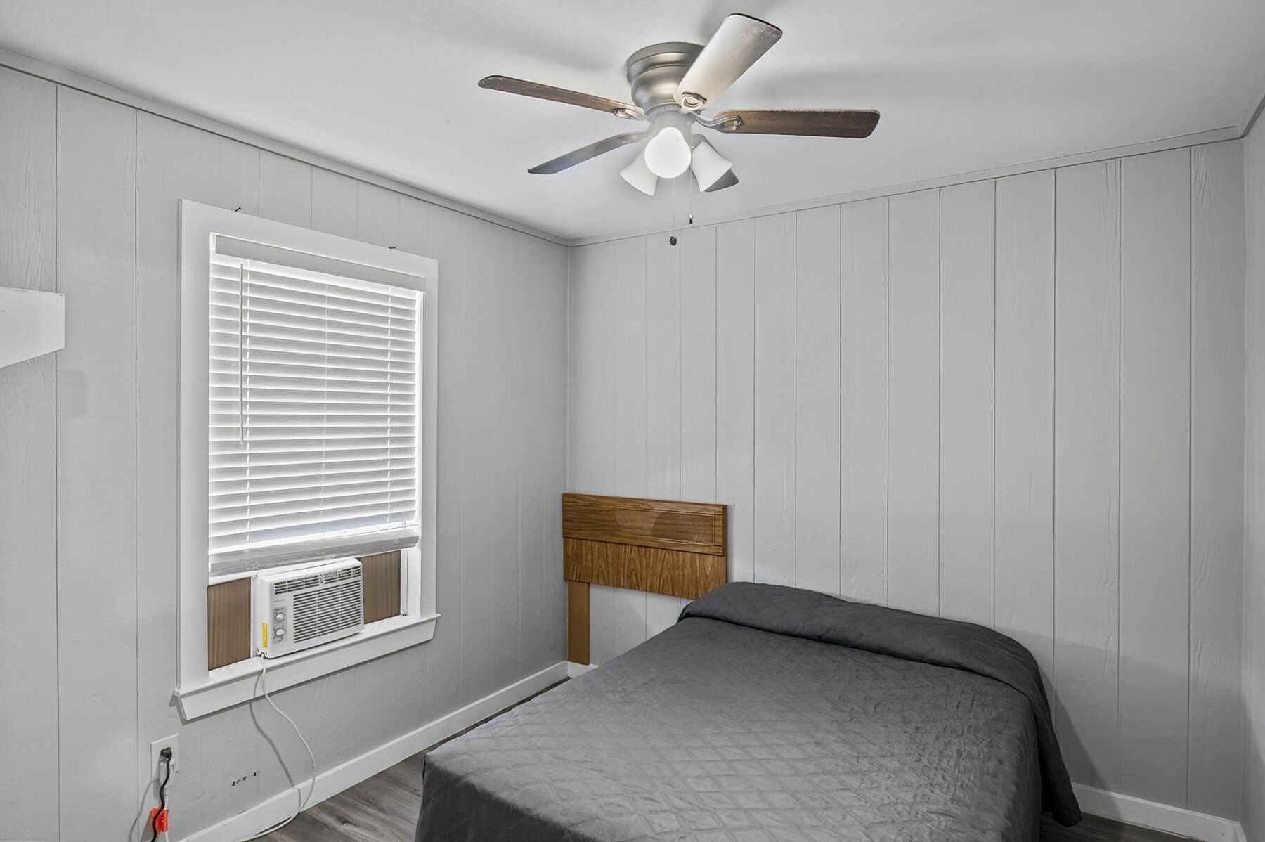 A bedroom with a bed, a ceiling fan, a window with blinds, and an air conditioning unit.
