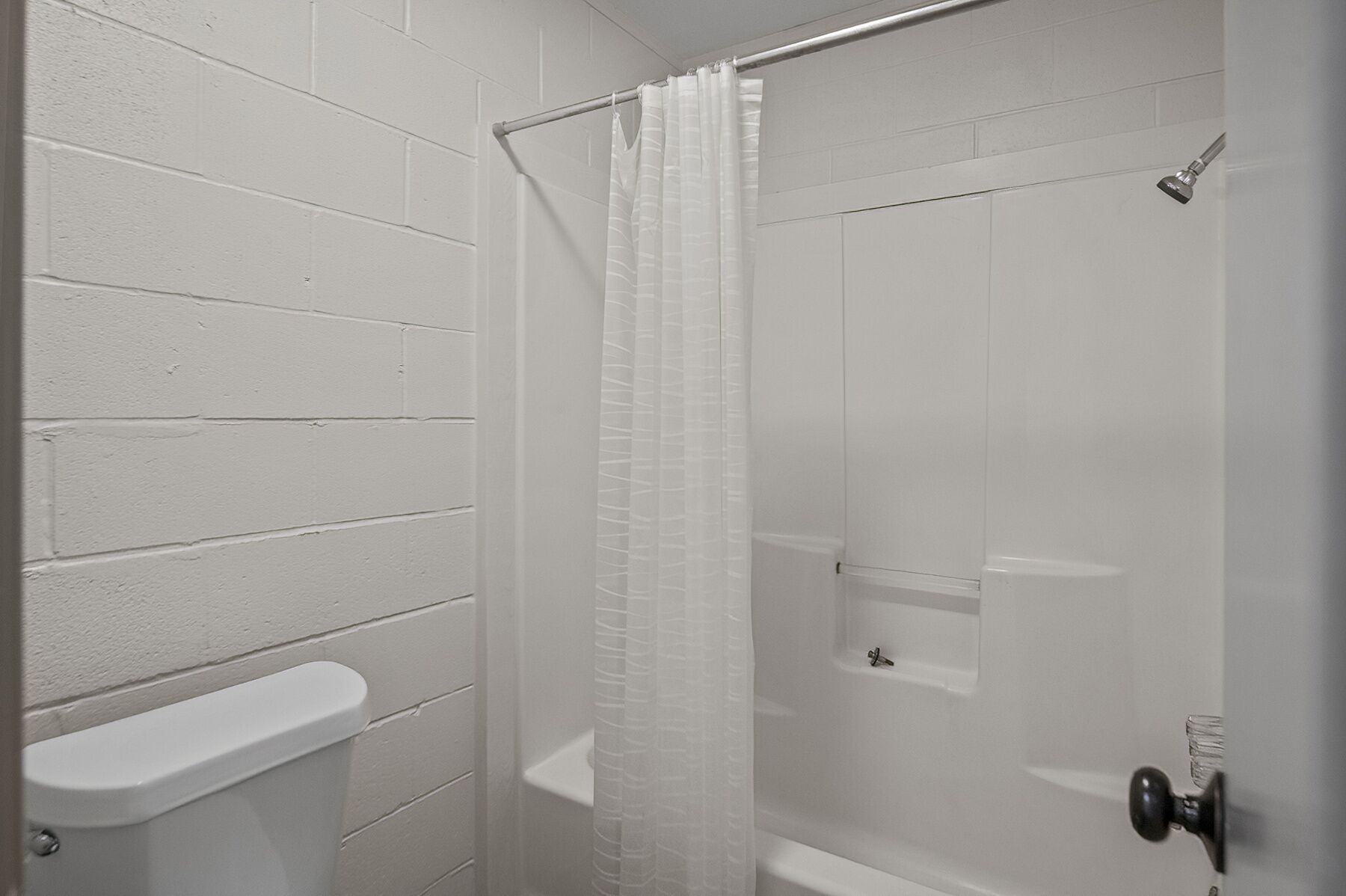 Eine weiße Ziegelwand, eine Dusche mit Glastür und eine weiße Toilette.