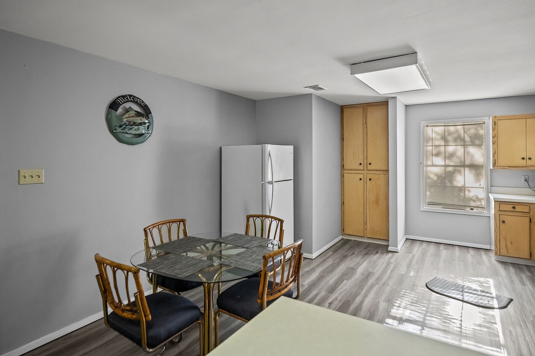 A compact kitchen with a dining area, featuring a glass-top table, wooden chairs, a white refrigerator, and wooden cabinets.