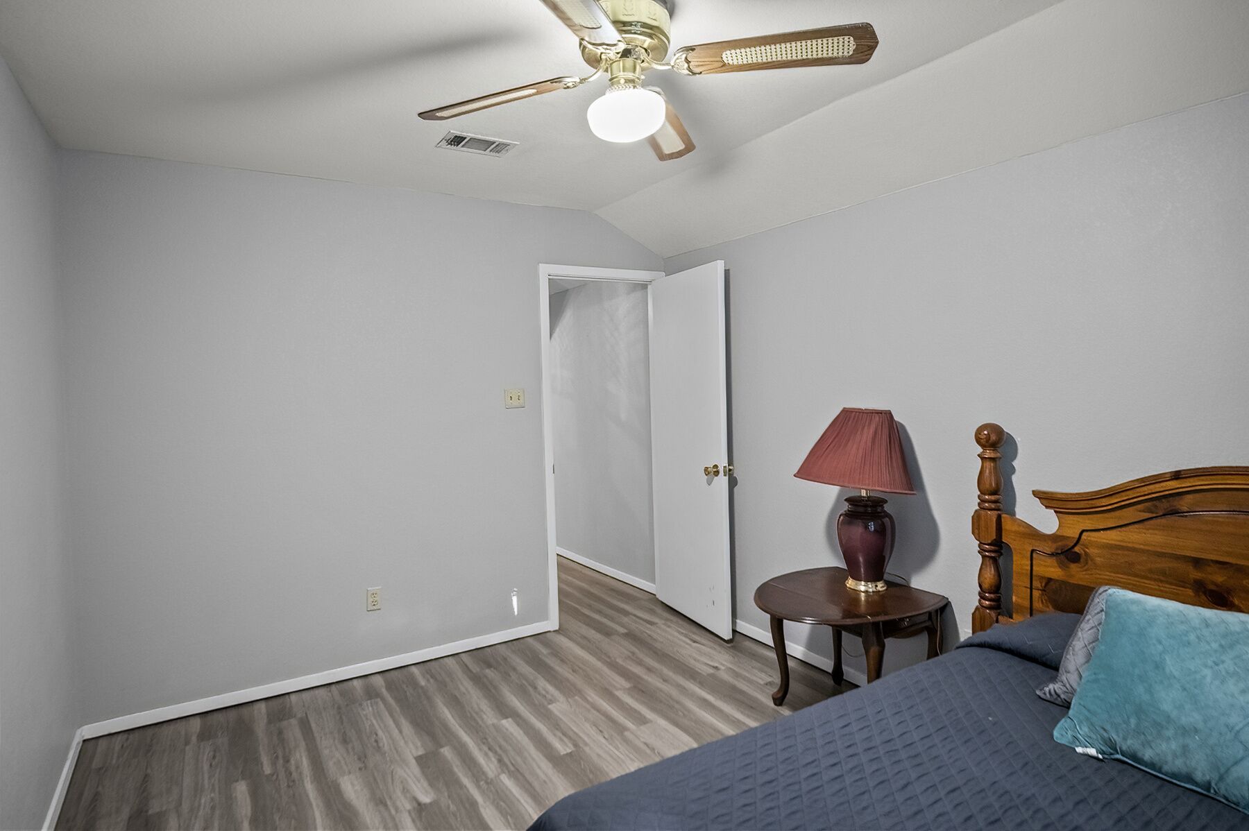 A bedroom with a bed, a nightstand, a lamp, a wooden headboard, and a ceiling fan.