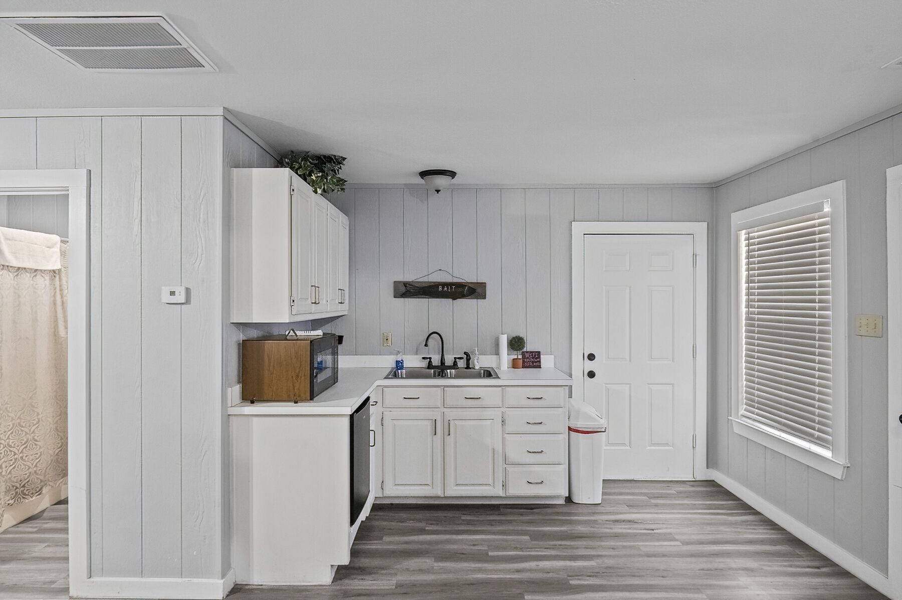 Una cocina compacta con armarios blancos, un microondas integrado y un lavabo.