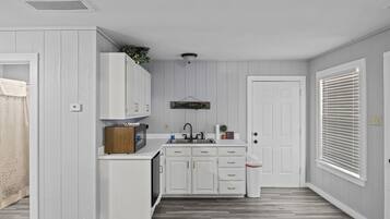 Una cocina compacta con armarios blancos, un microondas integrado y un lavabo.
