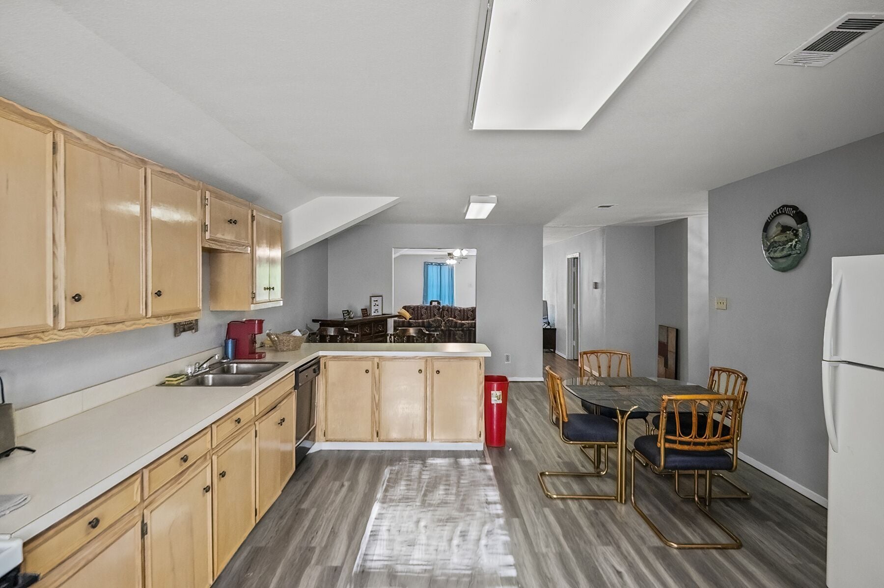 A compact kitchen with wooden cabinets, a dining area with two chairs, and a refrigerator.