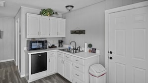 Une cuisine compacte avec des meubles blancs, un four à micro-ondes, une machine à café et un évier.