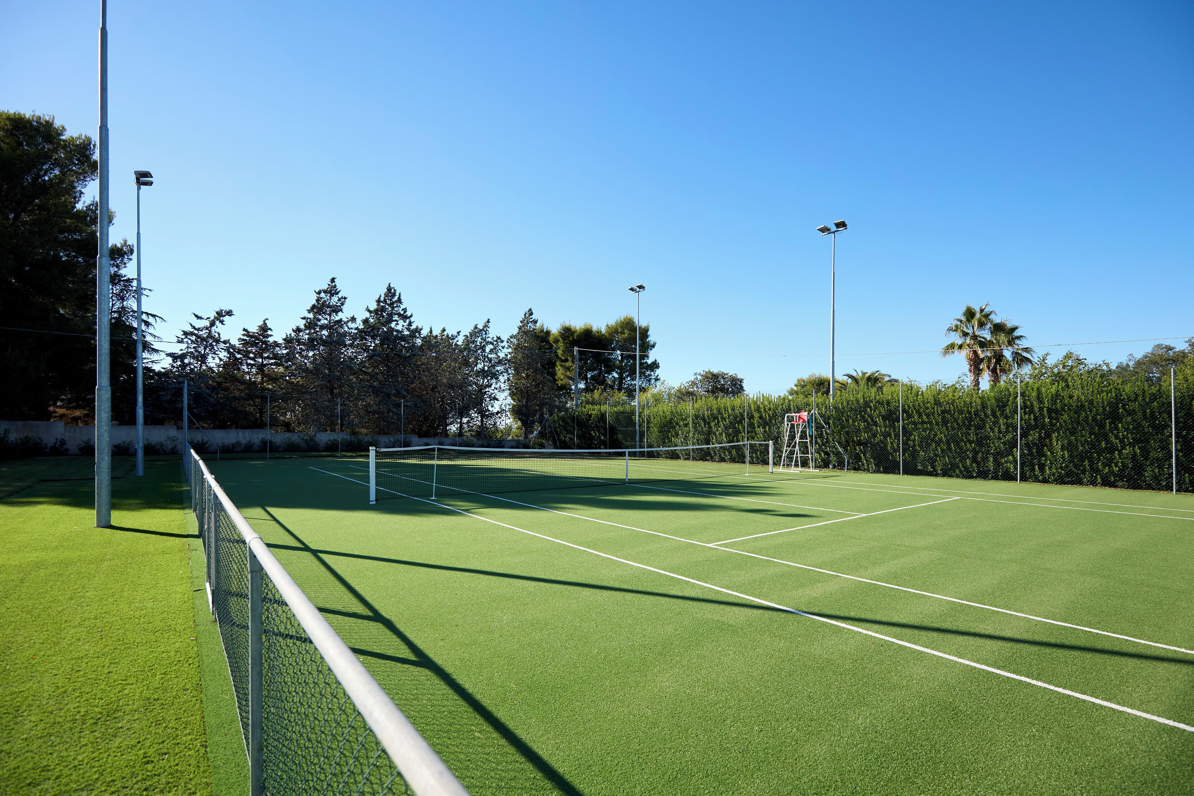 A tennis court with a net, surrounded by trees and a hedge.