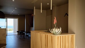 Un espace d’accueil avec un comptoir de réception en bois, un coin salon avec des chaises et une vue sur l’extérieur.
