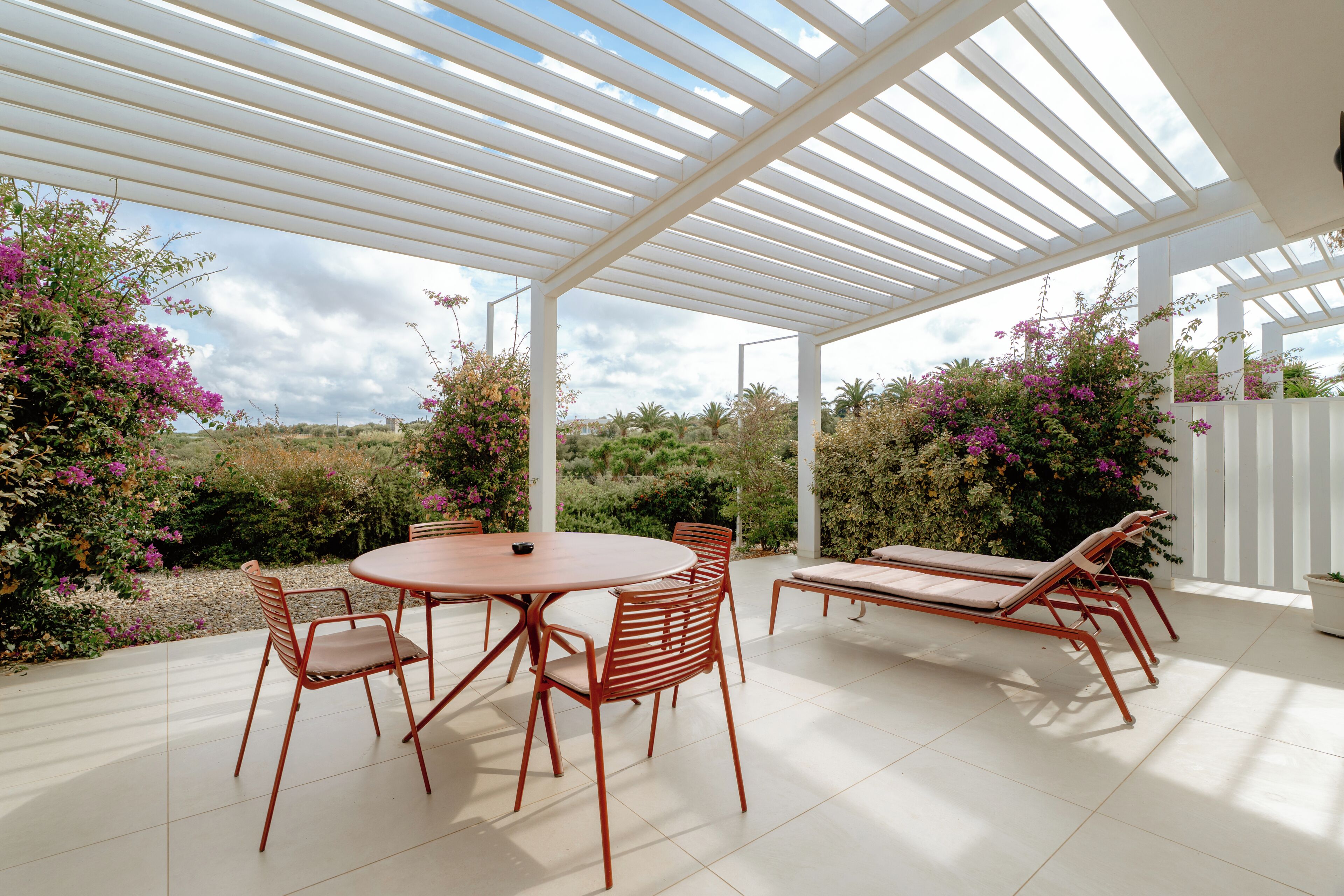 An outdoor patio with a round table and chairs, a sun lounger, and a white pergola structure.
