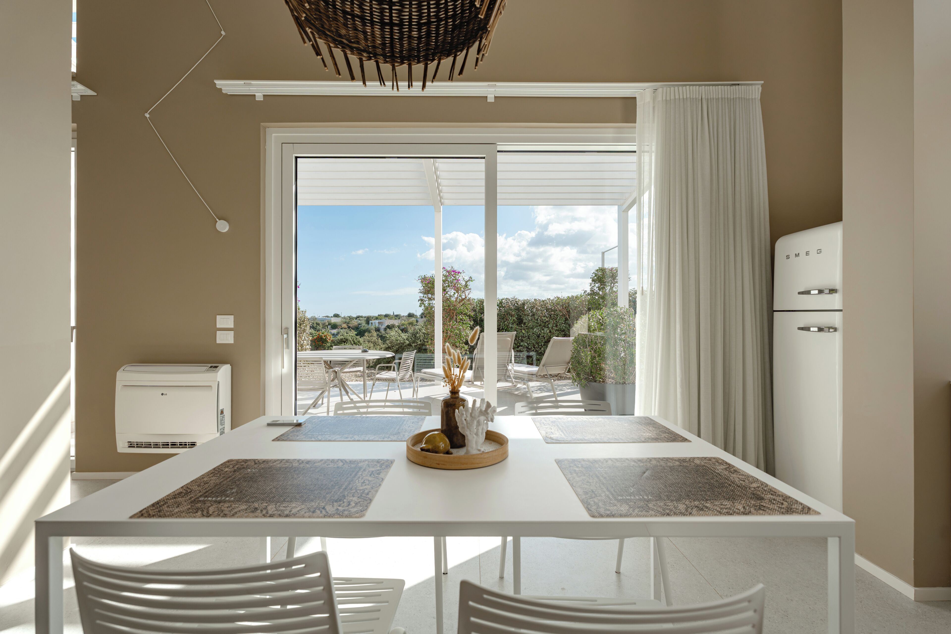 A modern dining area with a white table, chairs, and a view of the outdoors.