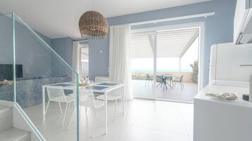 Een modern interieur met een glazen trap, een eetgedeelte met witte stoelen en een tafel, en uitzicht door een glazen deur op een terras.