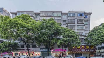 Un edificio a più piani con negozi al piano terra, una recinzione bianca in primo piano e alberi sullo sfondo.
