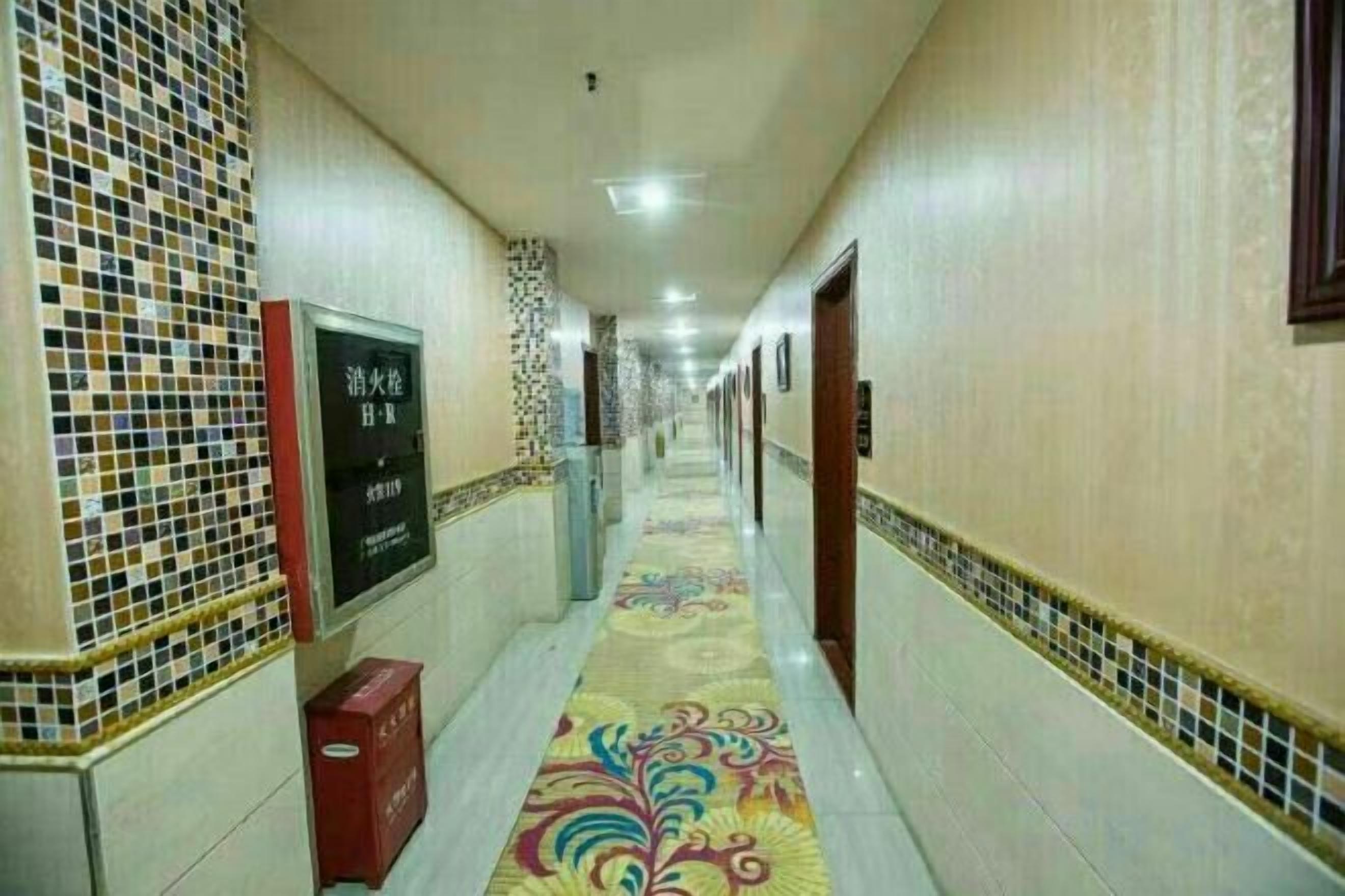 A hotel corridor with tiled walls, a patterned carpet, and a signboard.